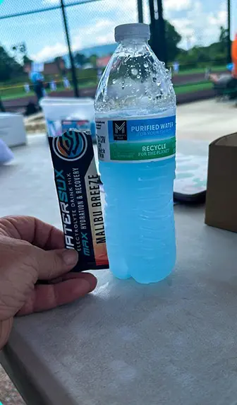 A person holding up a tooth paste and water bottle.